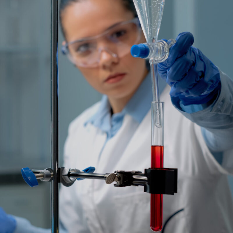Close up of scientist using laboratory glassware on desk for medical experiment. Biochemistry doctor mixing blood in test tube with solution from chemical dripping pipe for development